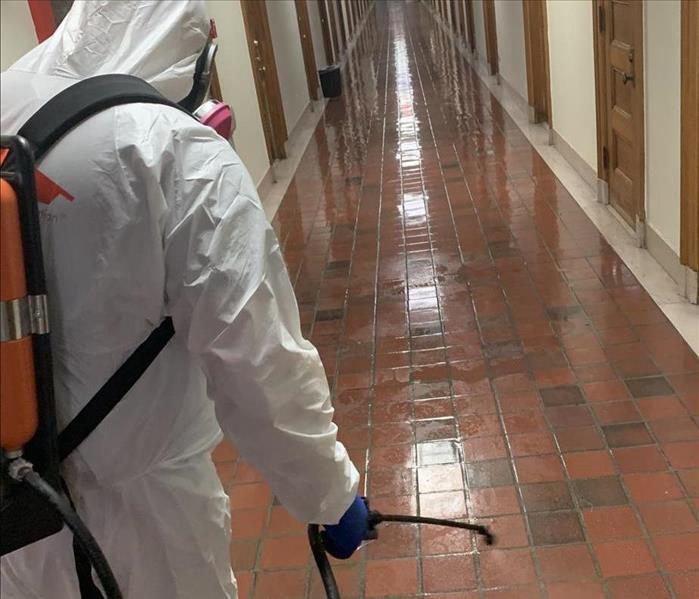 Technician in PPE spraying disinfection along floor